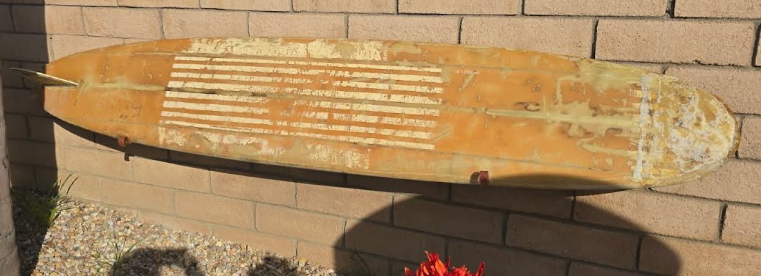 Faded classic Hobie longboard hanging on an outdoor block wall
